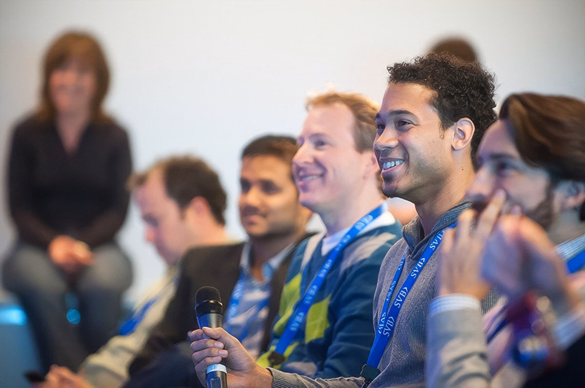 A group of smiling attendees at a corporate event in Boston, with one person holding a microphone.