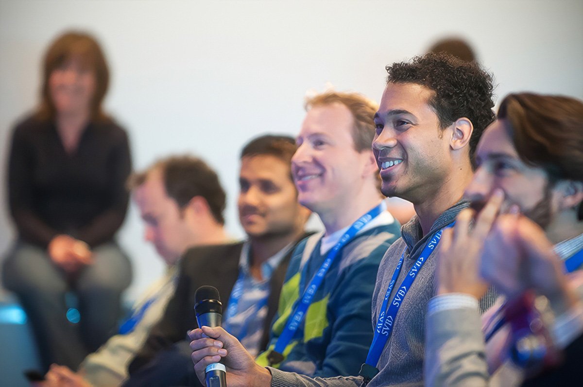 A group of smiling attendees at a corporate event in Boston, with one person holding a microphone.