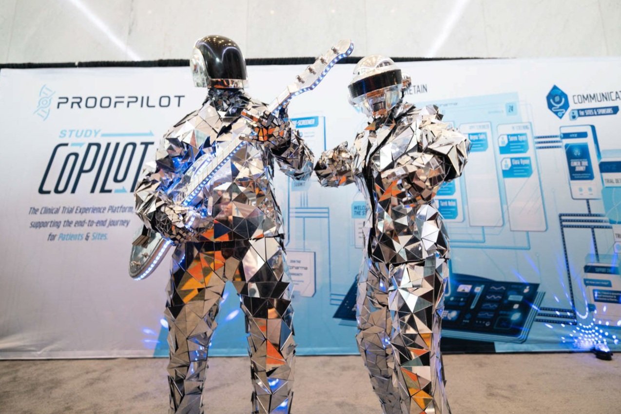 Two performers in reflective, geometric suits stand on display at a corporate event in Boston.