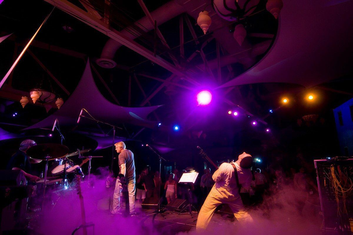 Musicians performing on stage with colorful lights and smoke.