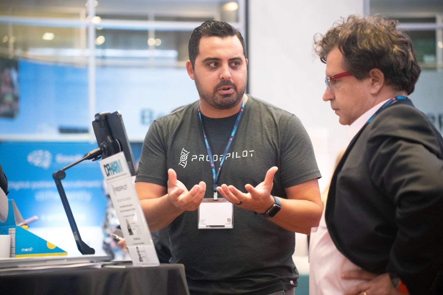Exhibitor gesturing while speaking with an attendee at a technology conference booth in Boston.
