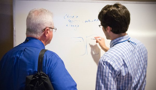 Two professionals discussing and writing on a whiteboard in a corporate setting.