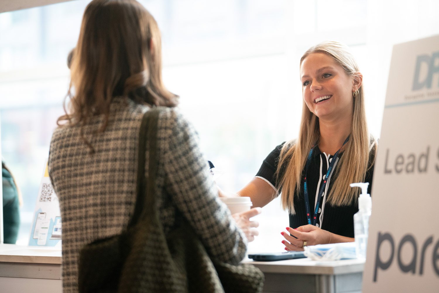 A corporate photographer in Boston capturing a smiling woman interacting with a client at a reception desk.
