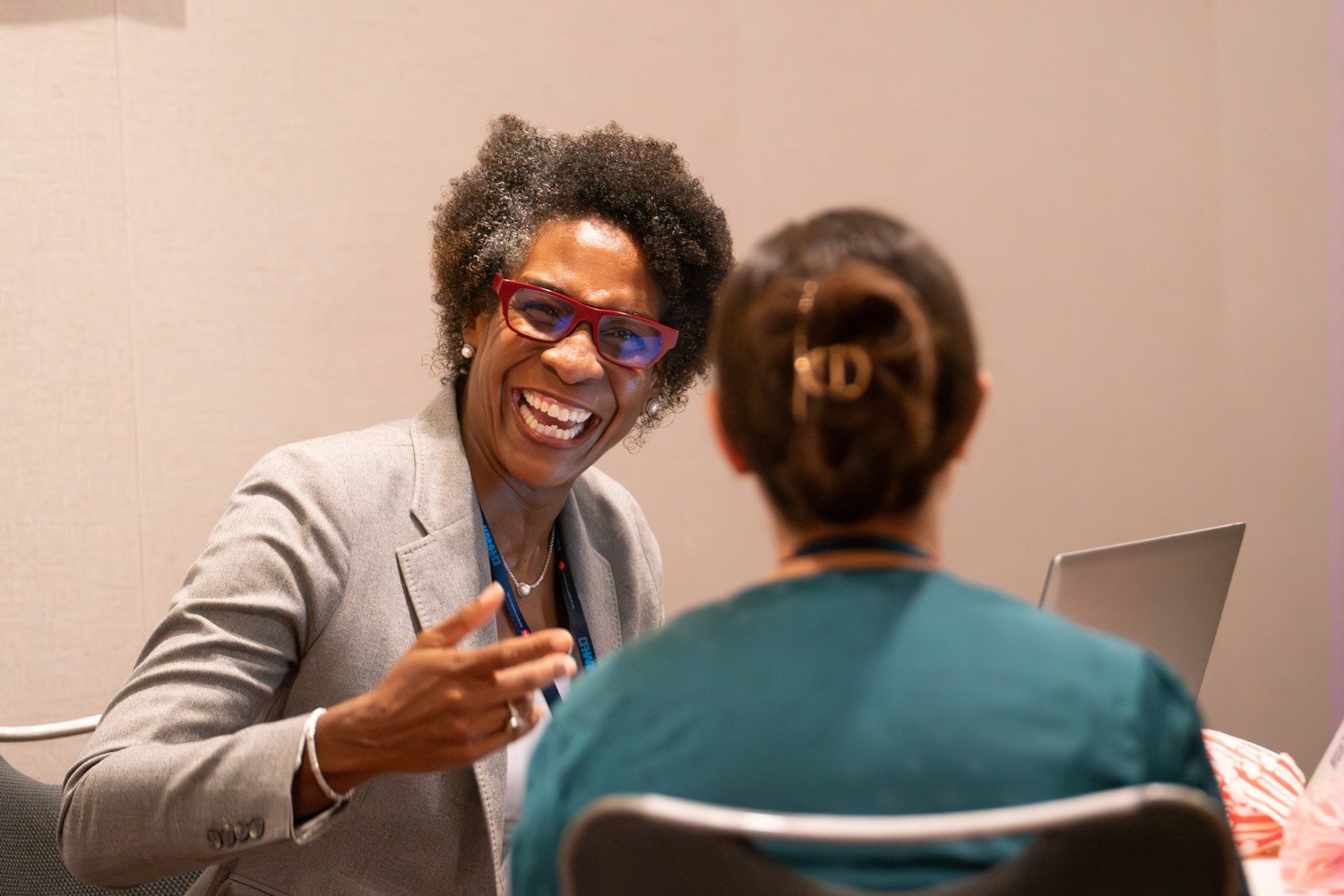 Two women engaged in a conversation in a corporate setting, with one smiling and gesturing.