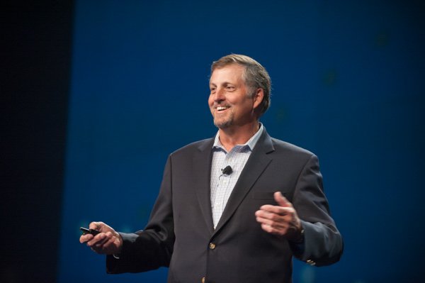 Speaker at a corporate event in Boston, presenting with a microphone and gesturing.