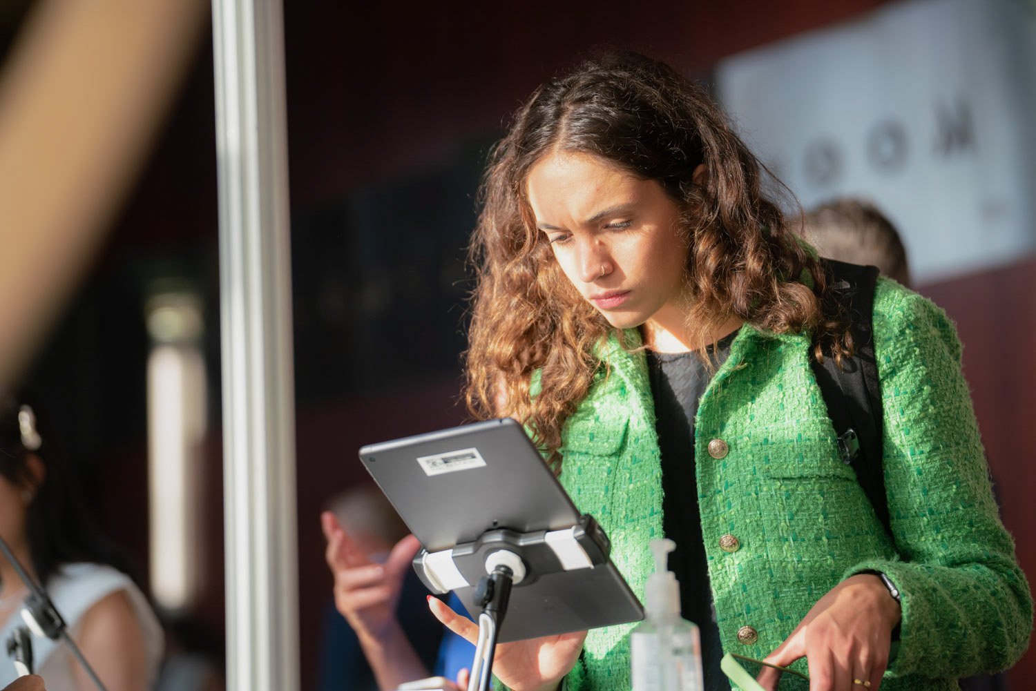 Woman in a green jacket using a tablet at a corporate event in Boston.