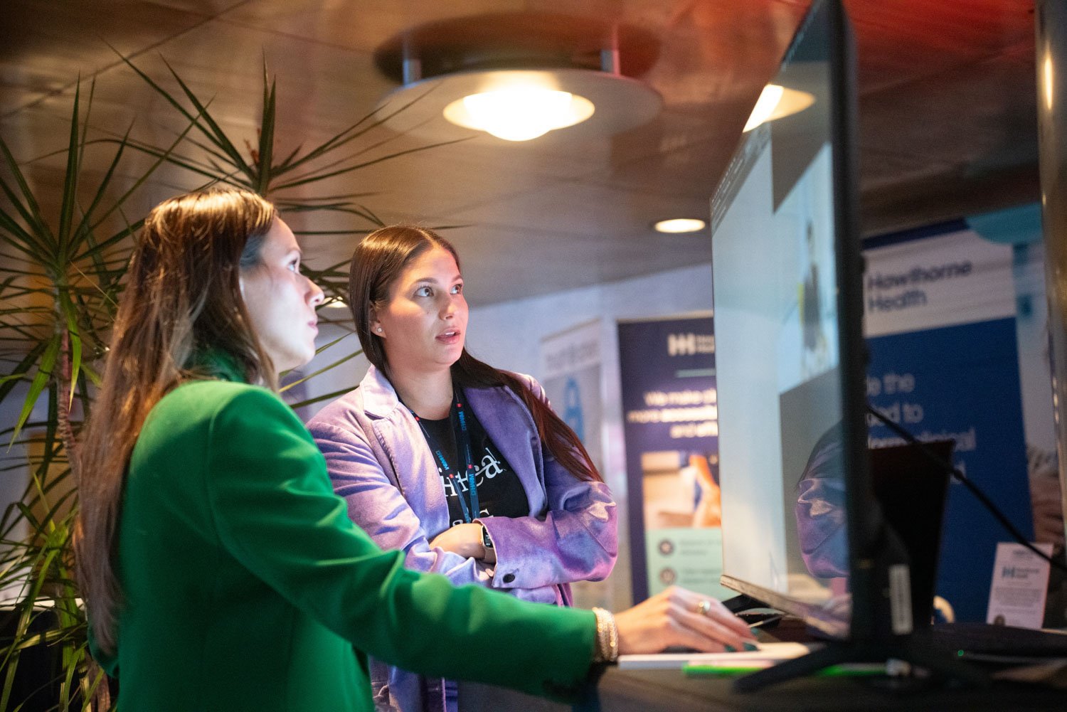 Two women engaged in discussion while viewing a screen at a corporate event in Boston.